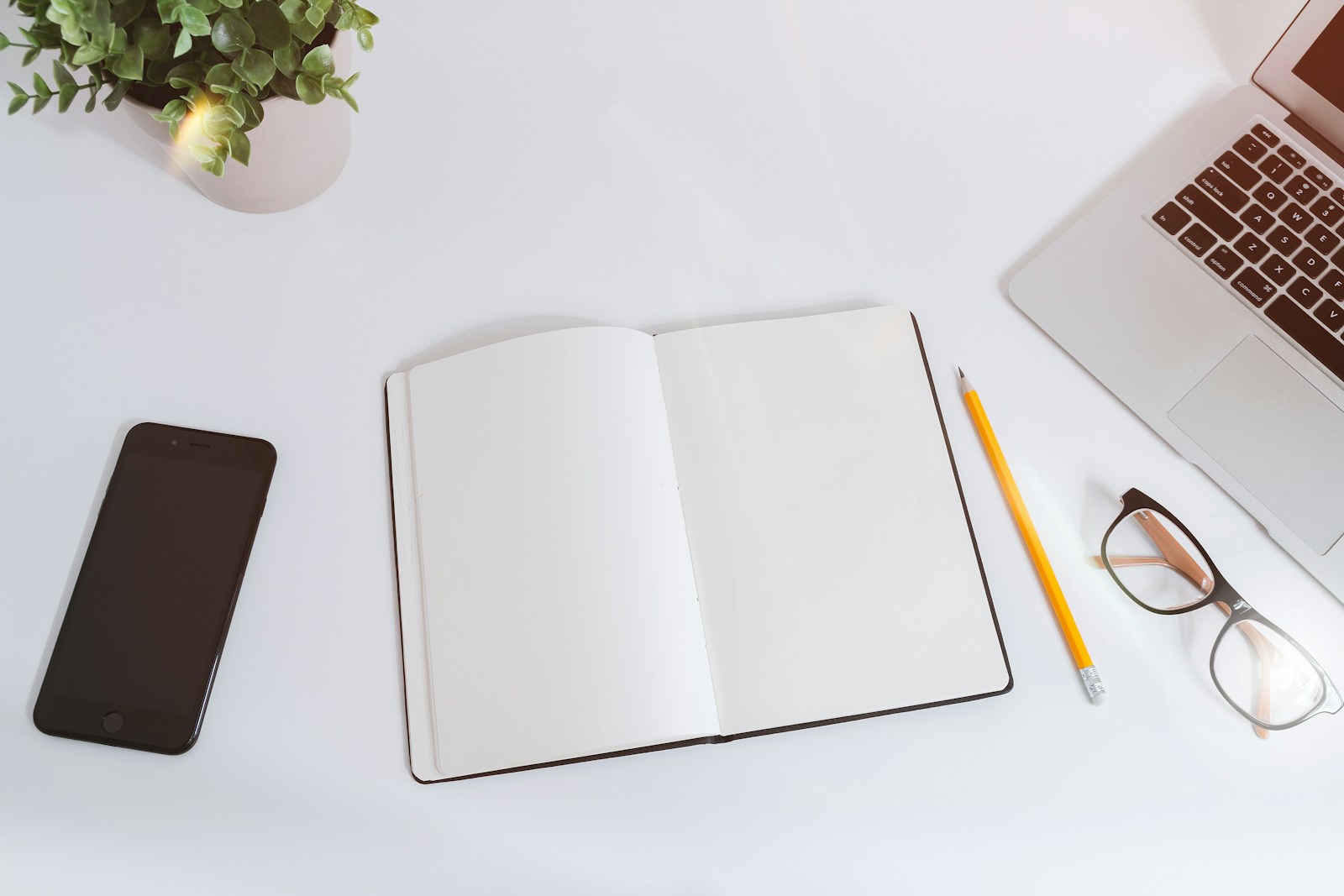 Open notebook, smartphone, and laptop on a white desk.