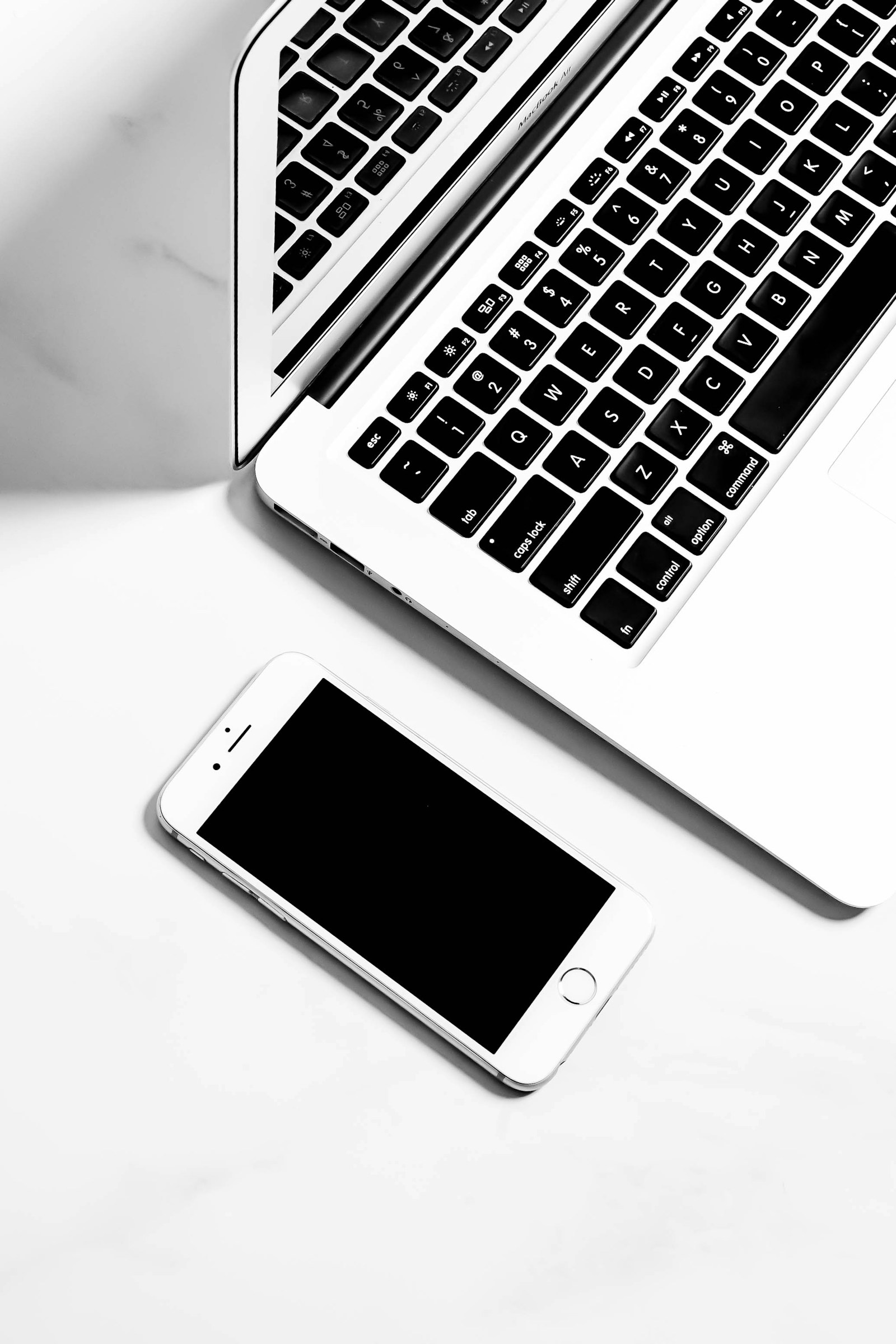 Laptop and smartphone with dark screens on a white tabletop.